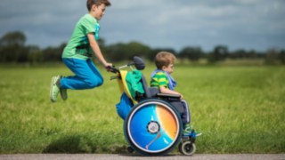 Zwei Jungs sind auf einer grünen Wiese unterwegs, einer davon sitzt im Rollstuhl und ist MPS-Betroffener